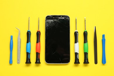 Damaged smartphone and repair tool set on yellow background, flat lay
