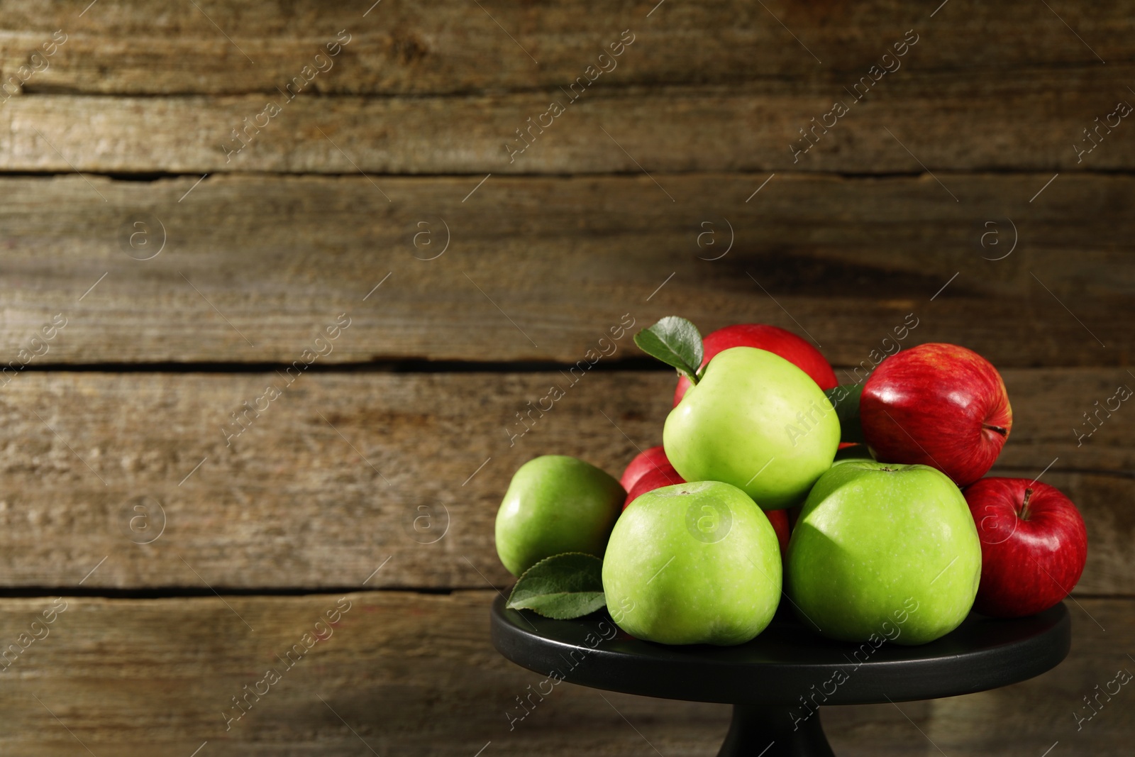 Photo of Stand with ripe red and green apples near wooden wall. Space for text