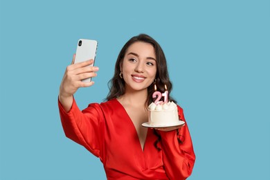 Photo of Coming of age party - 21st birthday. Woman holding cake with number shaped candles and taking selfie against light blue background