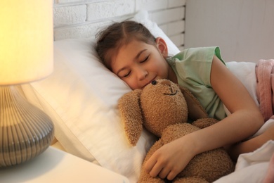 Photo of Cute child with stuffed bunny resting in bed at hospital