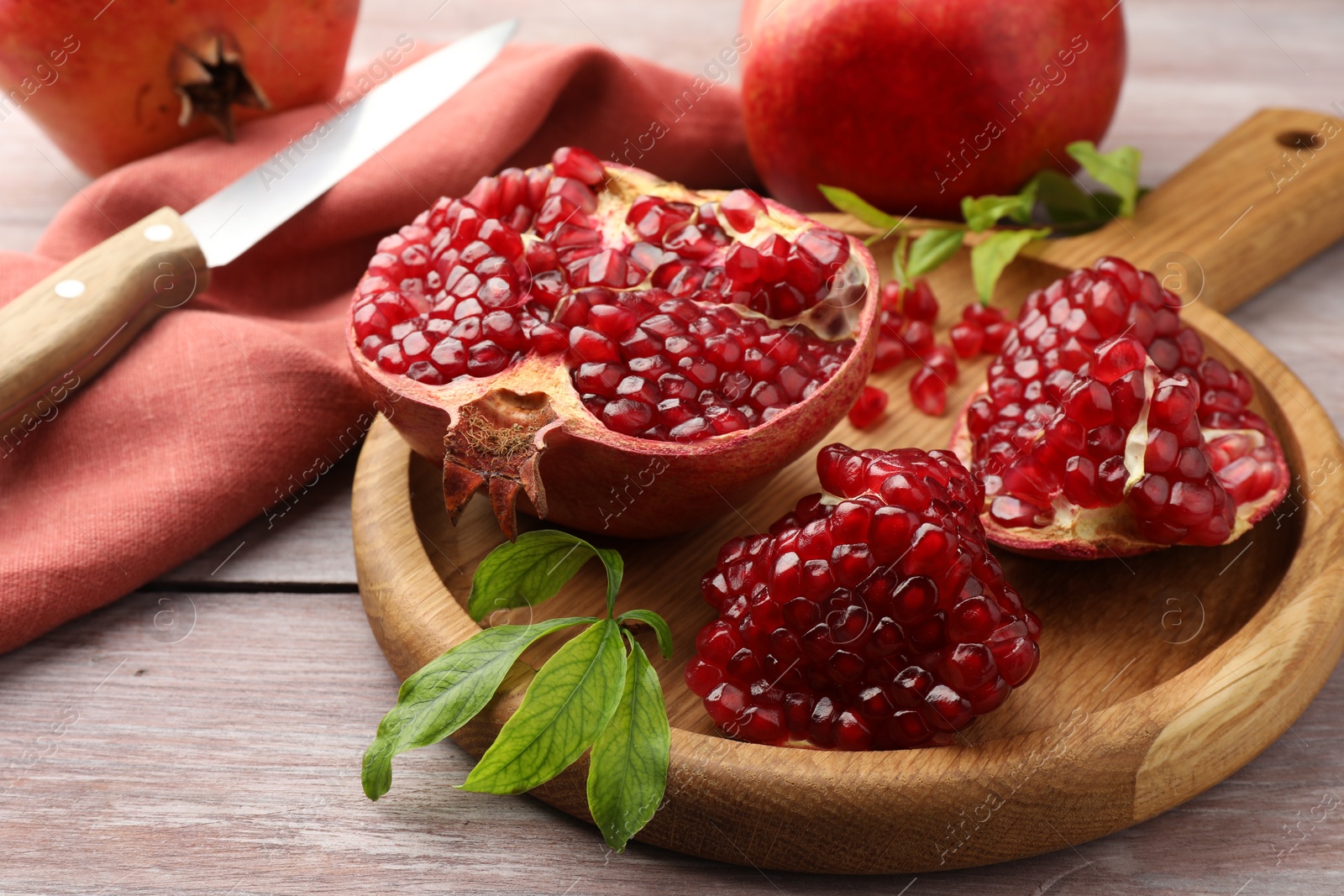 Photo of Fresh pomegranates, green leaves and knife on wooden table, closeup