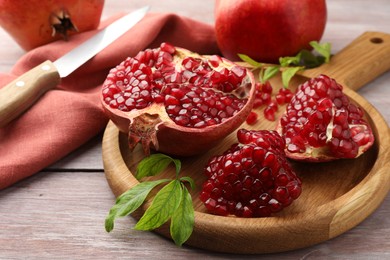 Photo of Fresh pomegranates, green leaves and knife on wooden table, closeup