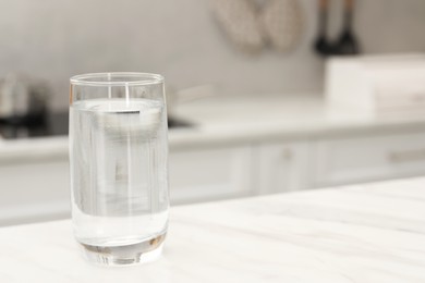 Photo of Glass with clear water on white marble table in kitchen, space for text