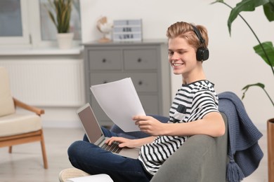 Online learning. Smiling teenage boy with laptop looking on essay at home