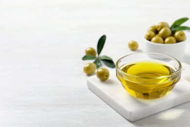 Photo of Glass bowl with fresh olive oil on white wooden table, space for text