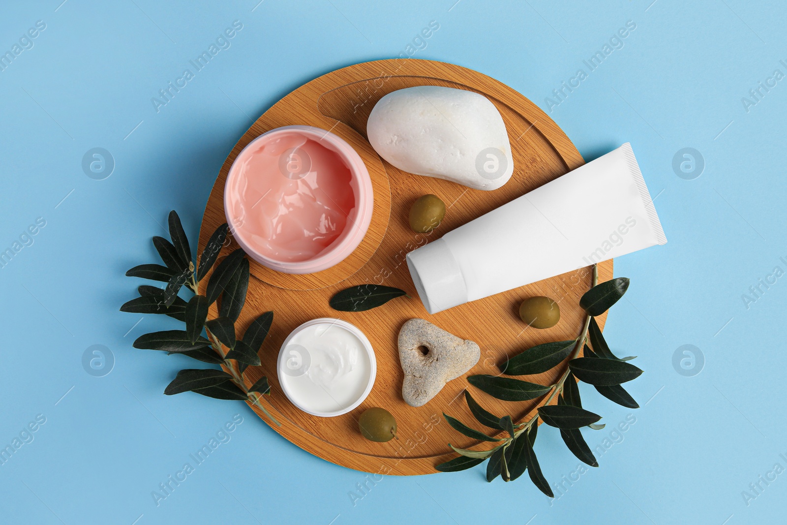 Photo of Different cosmetic products with olives and stones on light blue background, top view