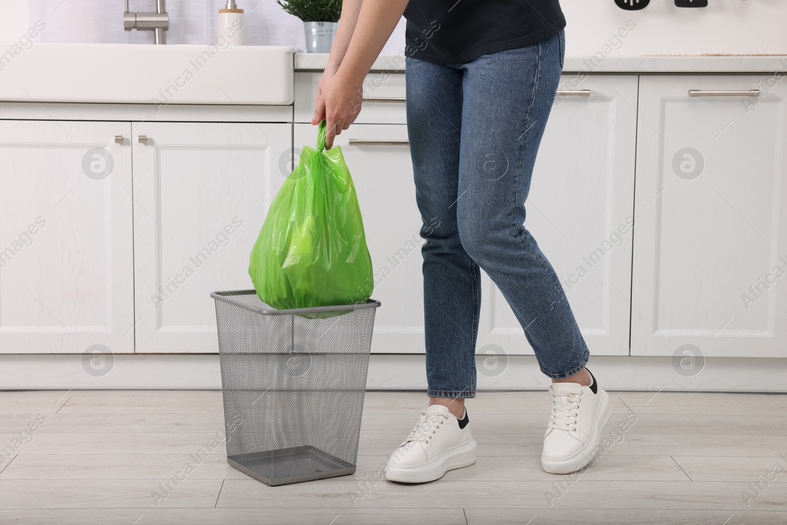 Photo of Woman taking garbage bag out of trash bin in kitchen, closeup