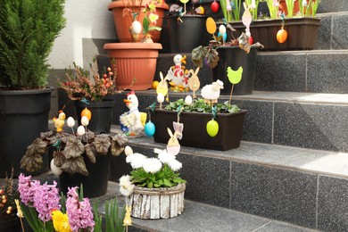 Beautiful plants with decorative eggs and different figures on stairs outdoors. Easter celebration