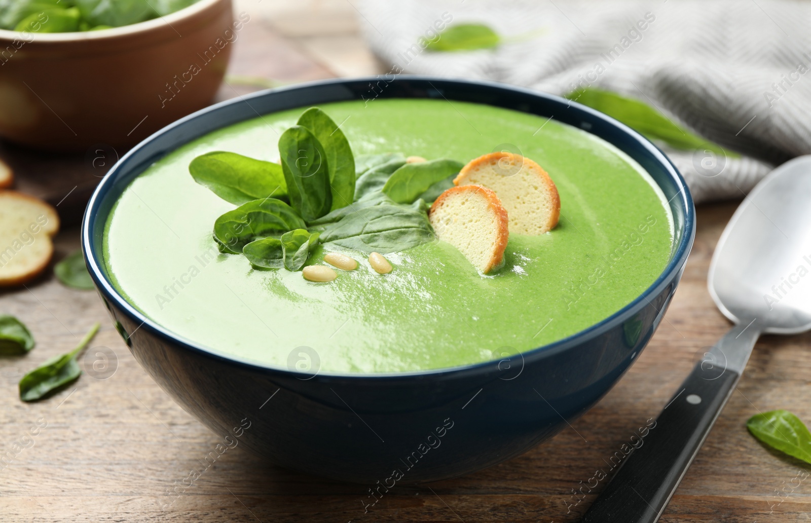 Photo of Bowl of healthy green soup with fresh spinach on wooden table