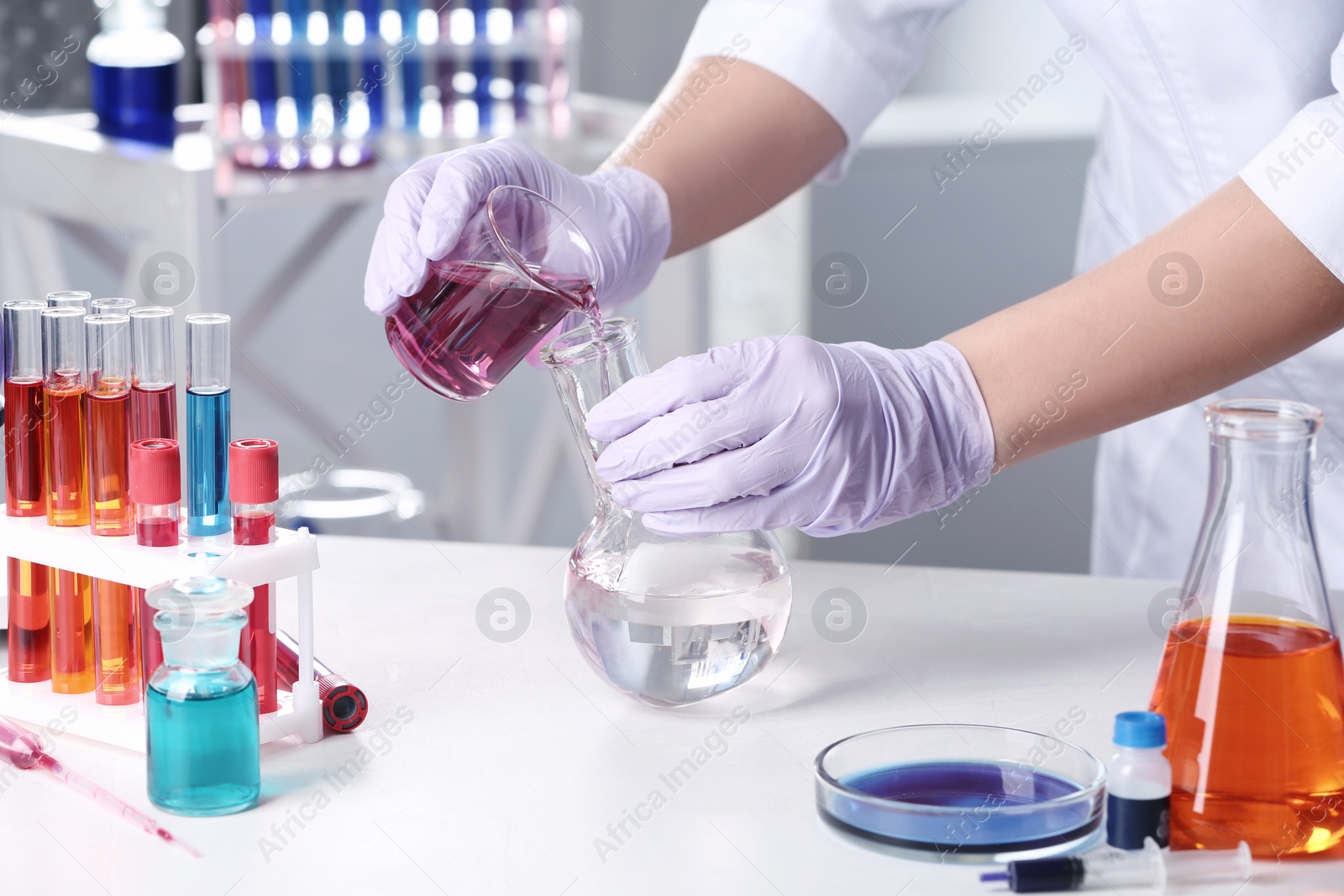 Photo of Scientist pouring reagent into flask at table in chemistry laboratory