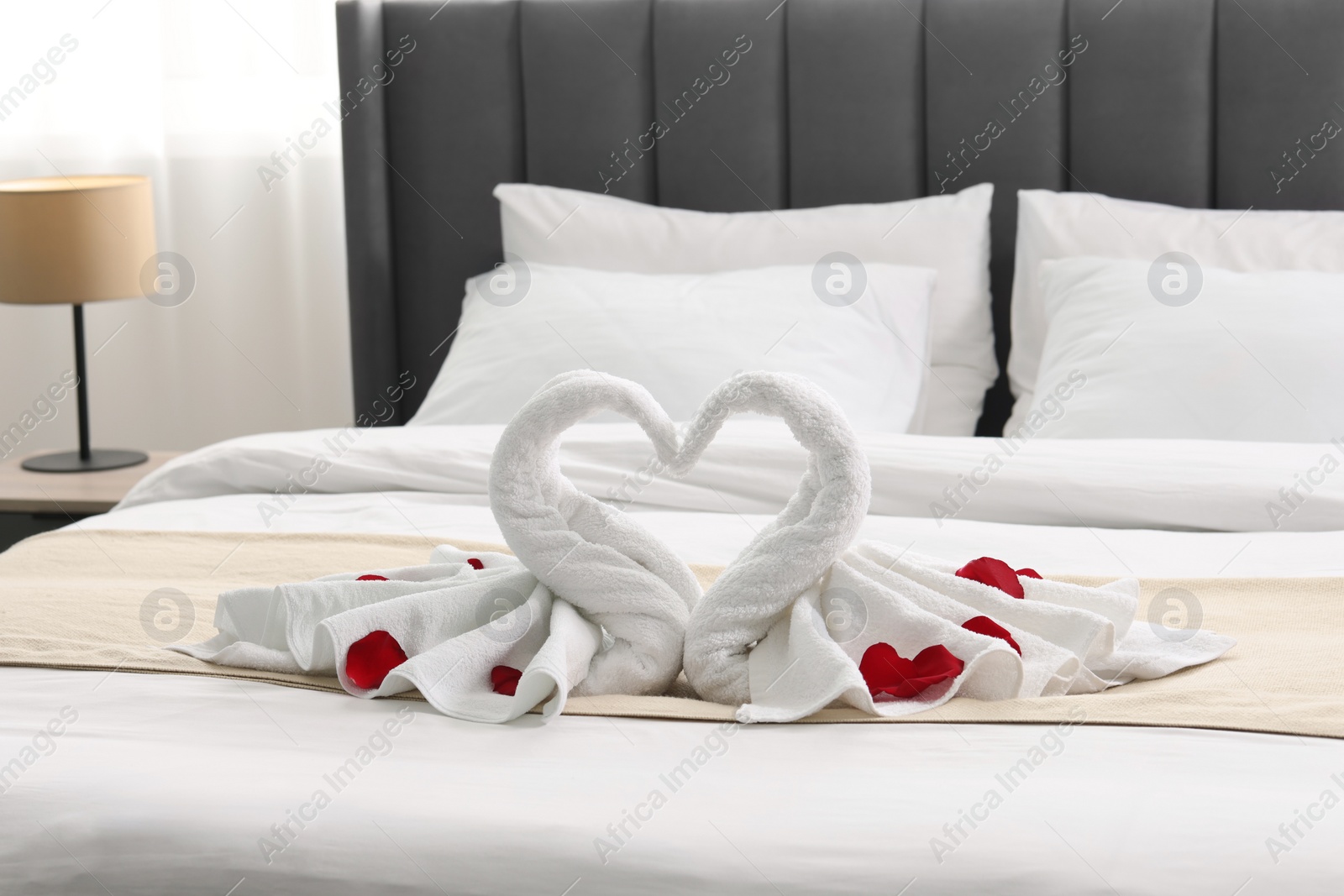 Photo of Honeymoon. Swans made of towels and rose petals on bed in room