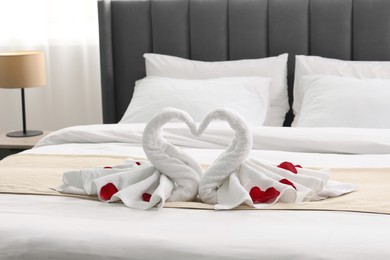 Honeymoon. Swans made of towels and rose petals on bed in room