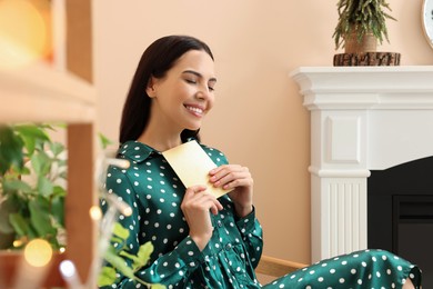 Happy woman holding Christmas greeting card in living room