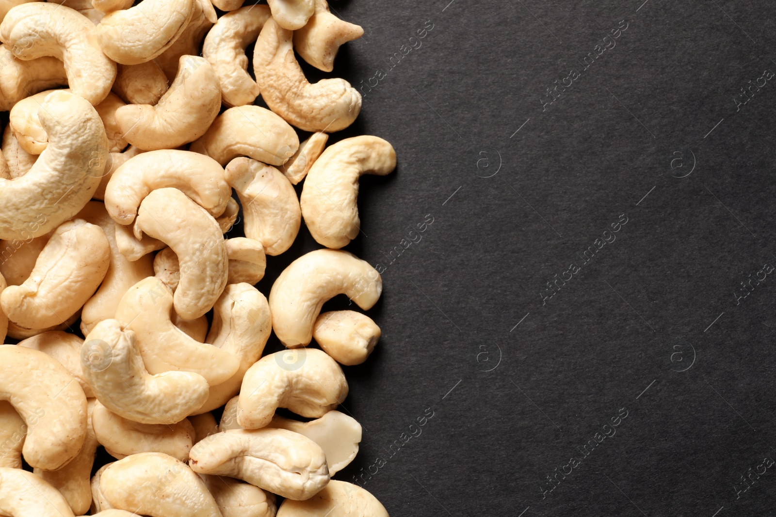 Photo of Tasty cashew nuts on black background, top view. Space for text