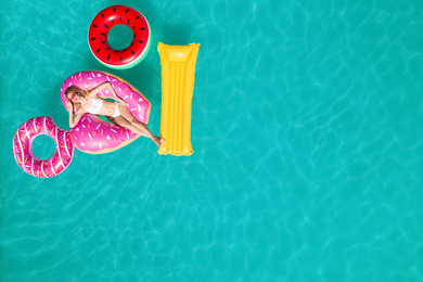 Image of Happy woman with inflatable mattress and rings in swimming pool, top view. Summer vacation