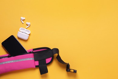 Photo of Stylish pink waist bag with smartphone and earphones on orange background, flat lay. Space for text