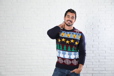 Portrait of happy man in Christmas sweater near white brick wall. Space for text