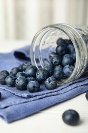 Overturned glass jar of ripe blueberries on white wooden table