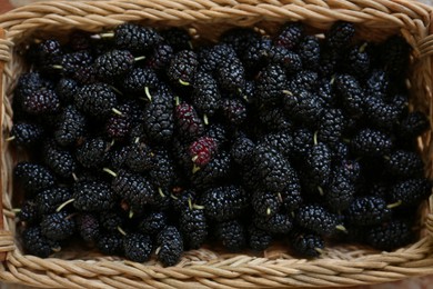 Photo of Wicker basket with delicious ripe black mulberries, top view