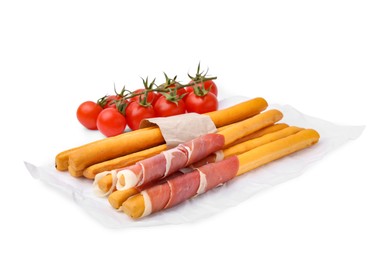 Delicious grissini sticks with prosciutto and tomatoes on white background