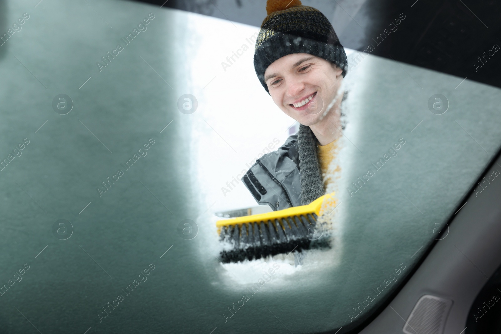 Photo of Man cleaning snow from car windshield, view from inside