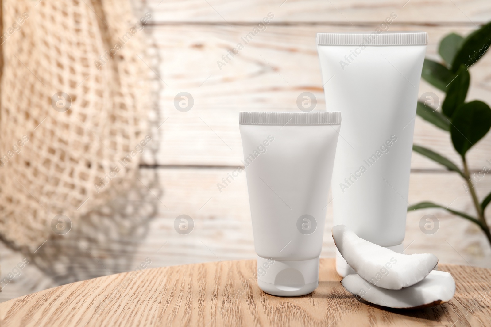 Photo of Tubes of hand cream and coconut pieces on wooden table, space for text