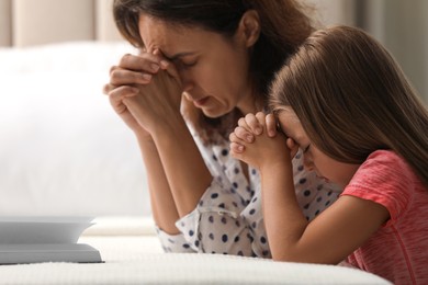 Photo of Mature woman with her little granddaughter praying together over Bible in bedroom