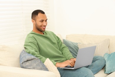African American man typing on laptop on sofa in room