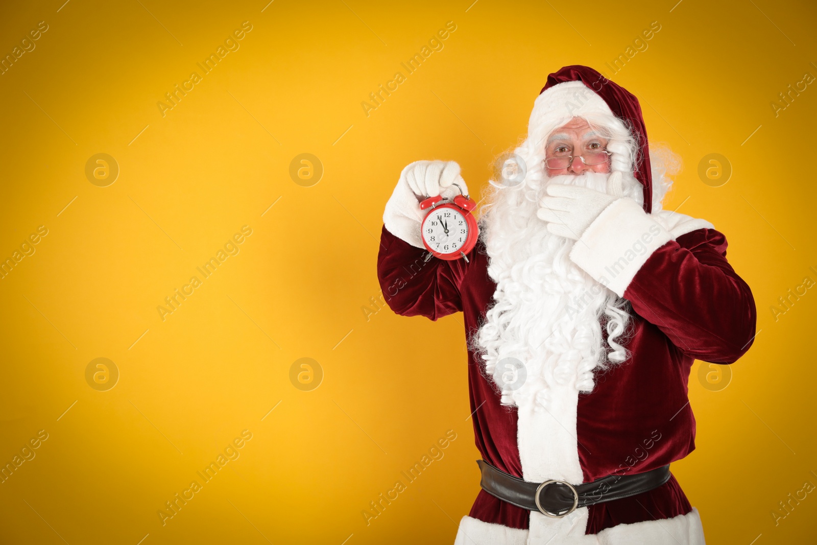 Photo of Santa Claus holding alarm clock on yellow background, space for text. Christmas countdown