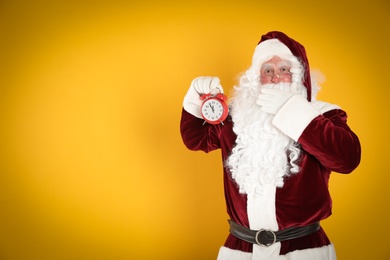 Santa Claus holding alarm clock on yellow background, space for text. Christmas countdown