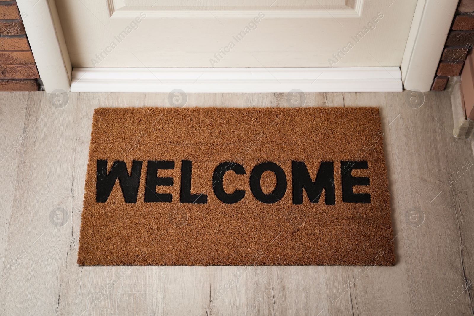 Photo of Door mat with word Welcome on wooden floor in hall, above view