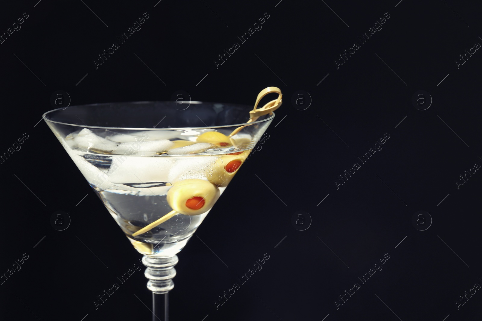 Photo of Martini cocktail with ice and olives on dark background, closeup. Space for text