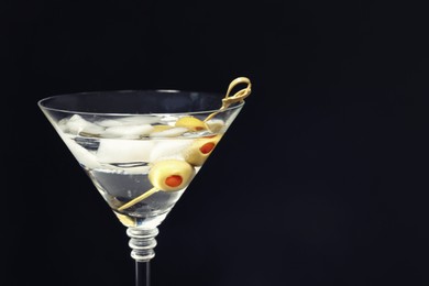 Photo of Martini cocktail with ice and olives on dark background, closeup. Space for text