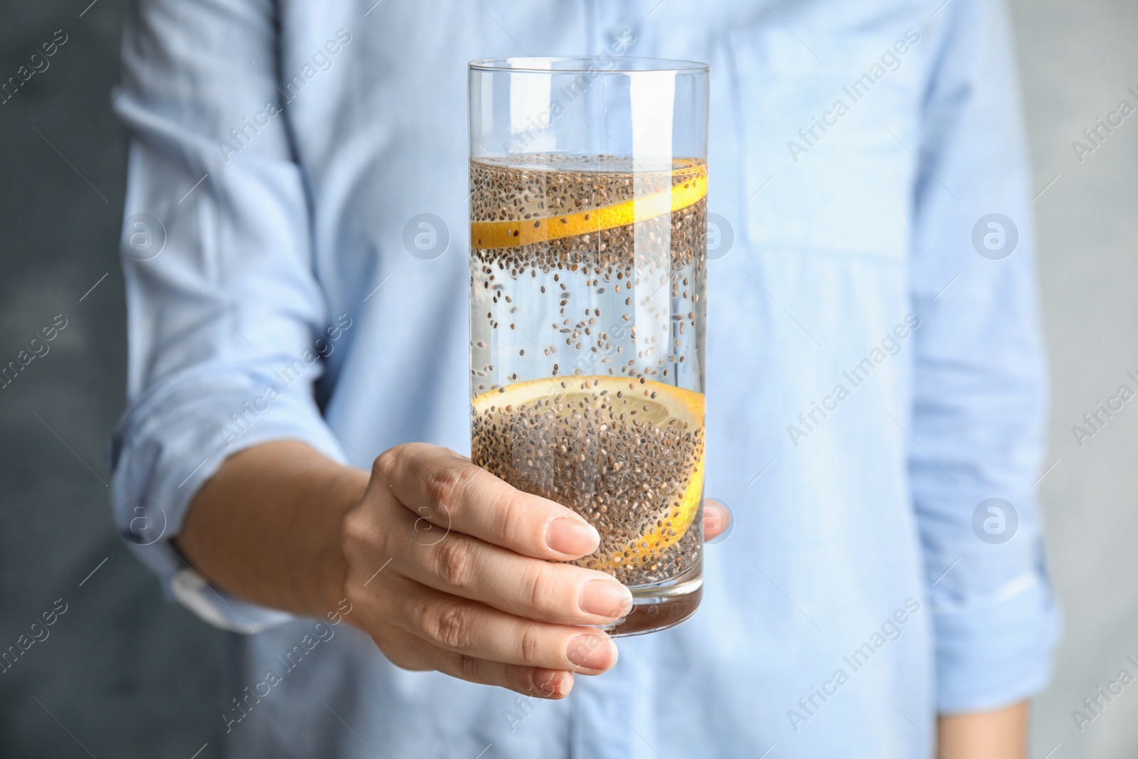 Photo of Woman holding glass of water with chia seeds on grey background, closeup