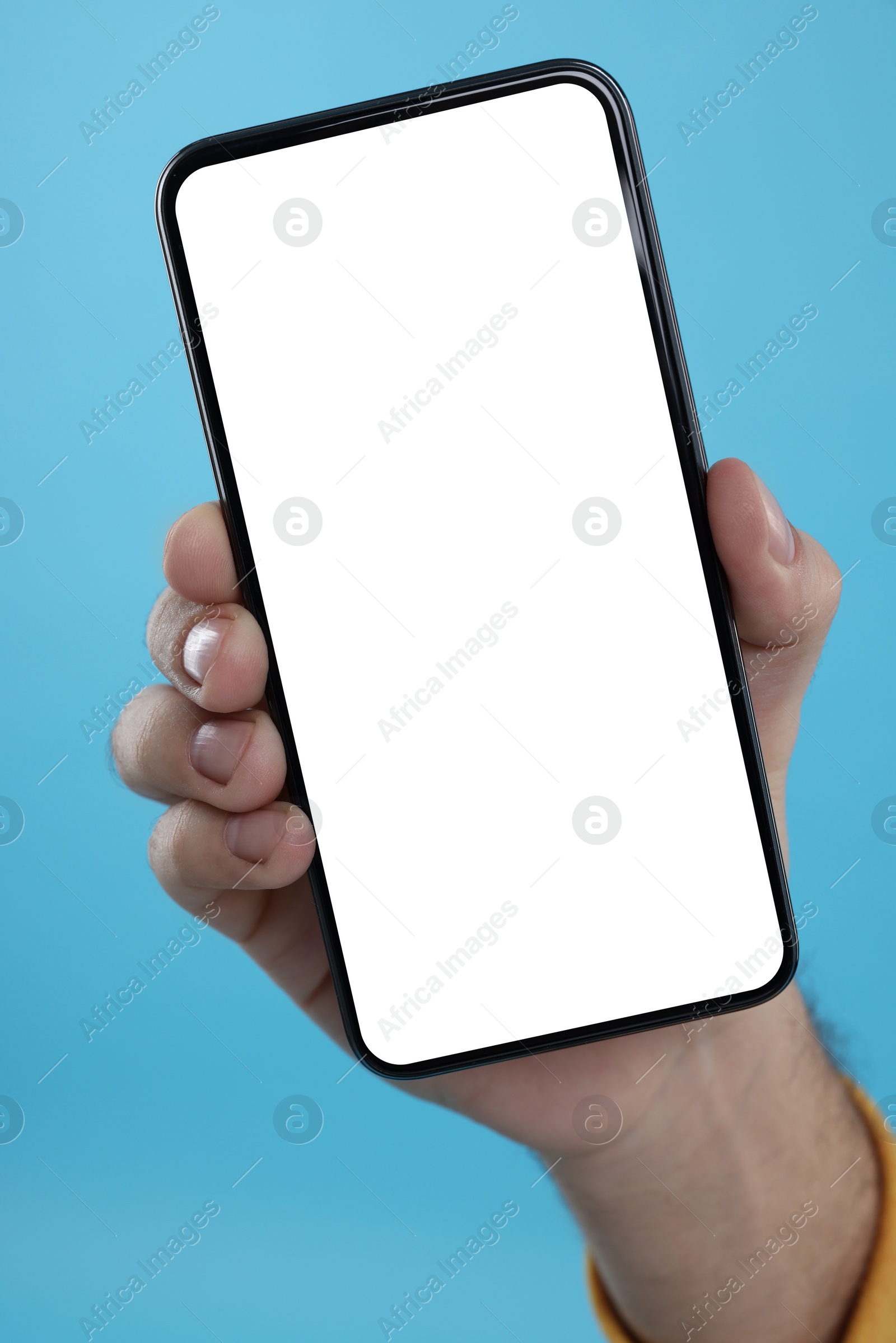 Photo of Man holding smartphone with blank screen on light blue background, closeup