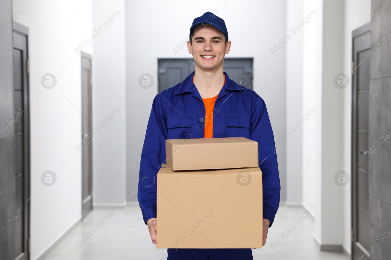 Photo of Young courier with cardboard boxes in hallway