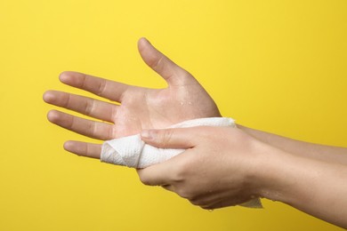 Woman wiping hands with paper towel on yellow background, closeup