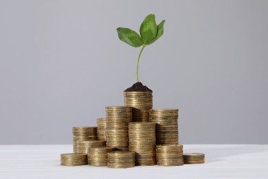Photo of Stacks of coins with green sprout on white table against grey background. Investment concept