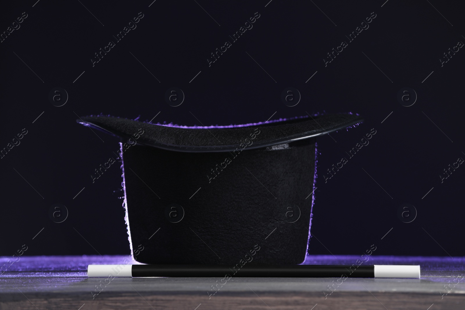 Photo of Magician's hat and wand on wooden table against black background