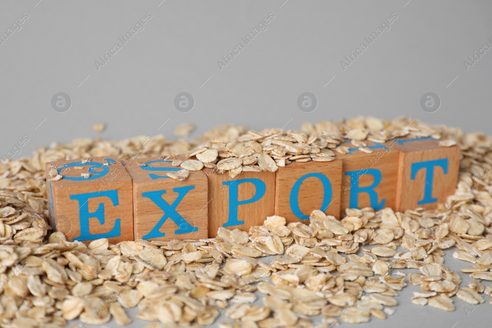 Photo of Pile of oatmeal and wooden cubes with word Export on grey background, closeup