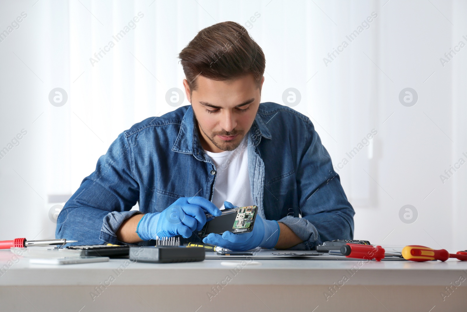 Photo of Technician repairing broken smartphone at table in workshop