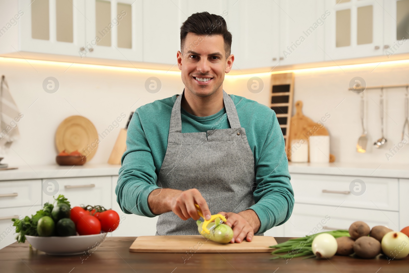 Photo of Man peeling zucchini at table in kitchen. Preparing vegetable