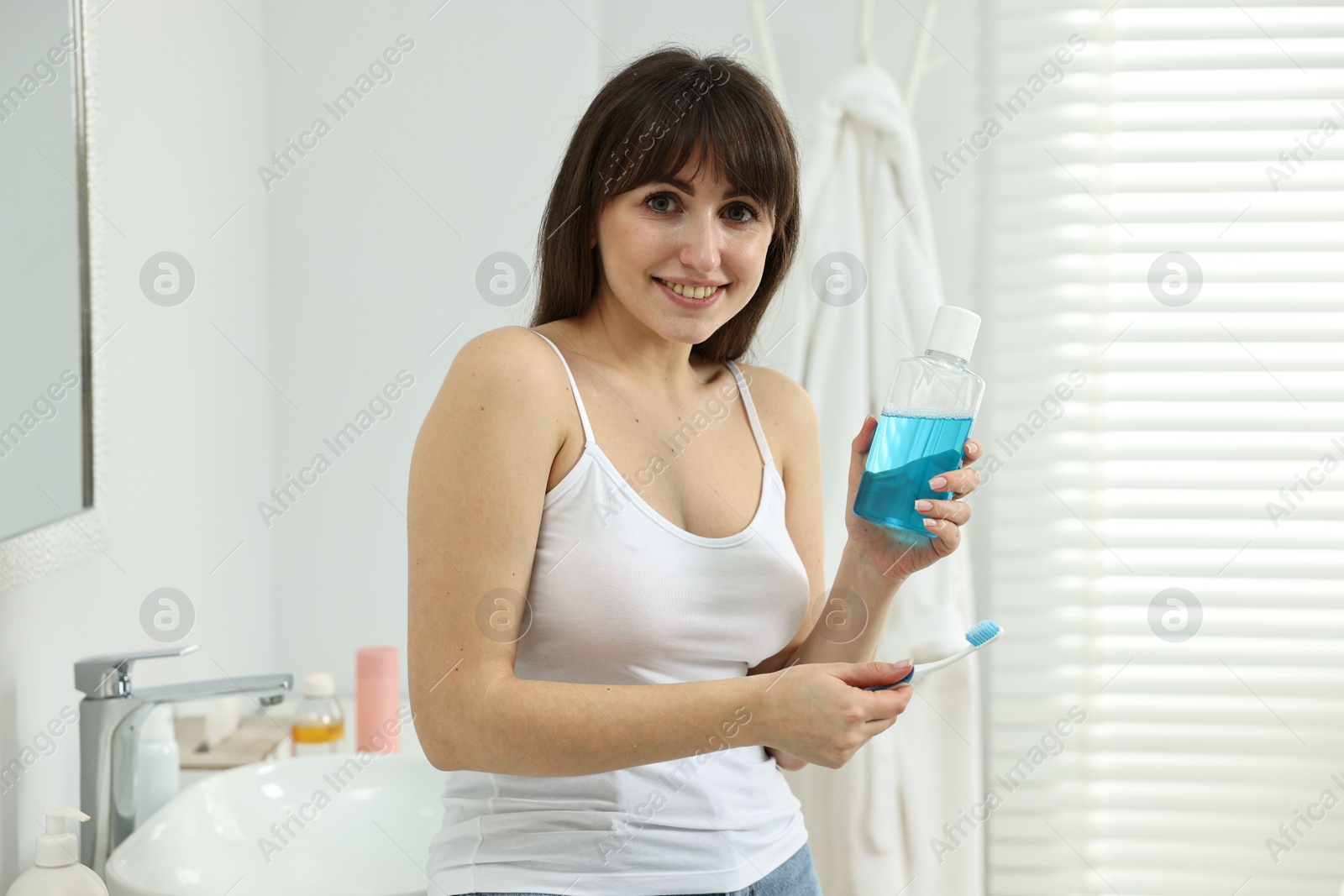 Photo of Young woman with mouthwash and toothbrush in bathroom