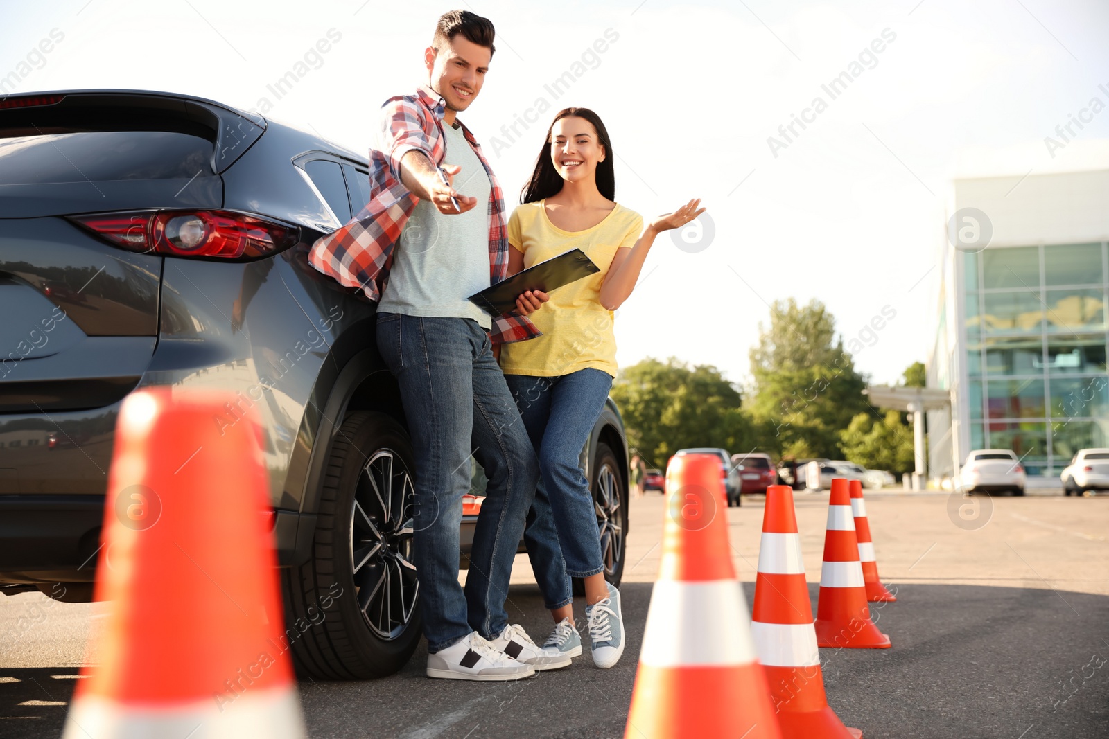 Photo of Instructor with clipboard and his student near car outdoors. Driving school exam