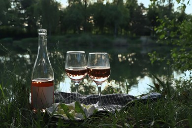 Photo of Delicious rose wine, cheese and grapes on picnic blanket near lake