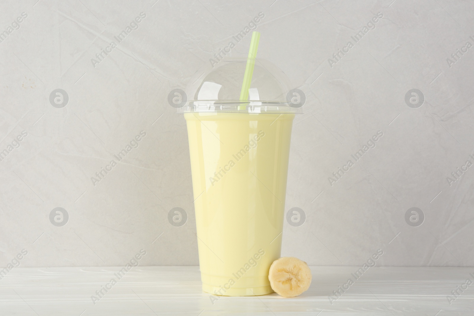 Photo of Plastic cup of tasty smoothie and fresh banana on white wooden table