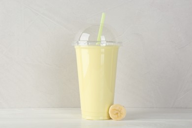 Photo of Plastic cup of tasty smoothie and fresh banana on white wooden table