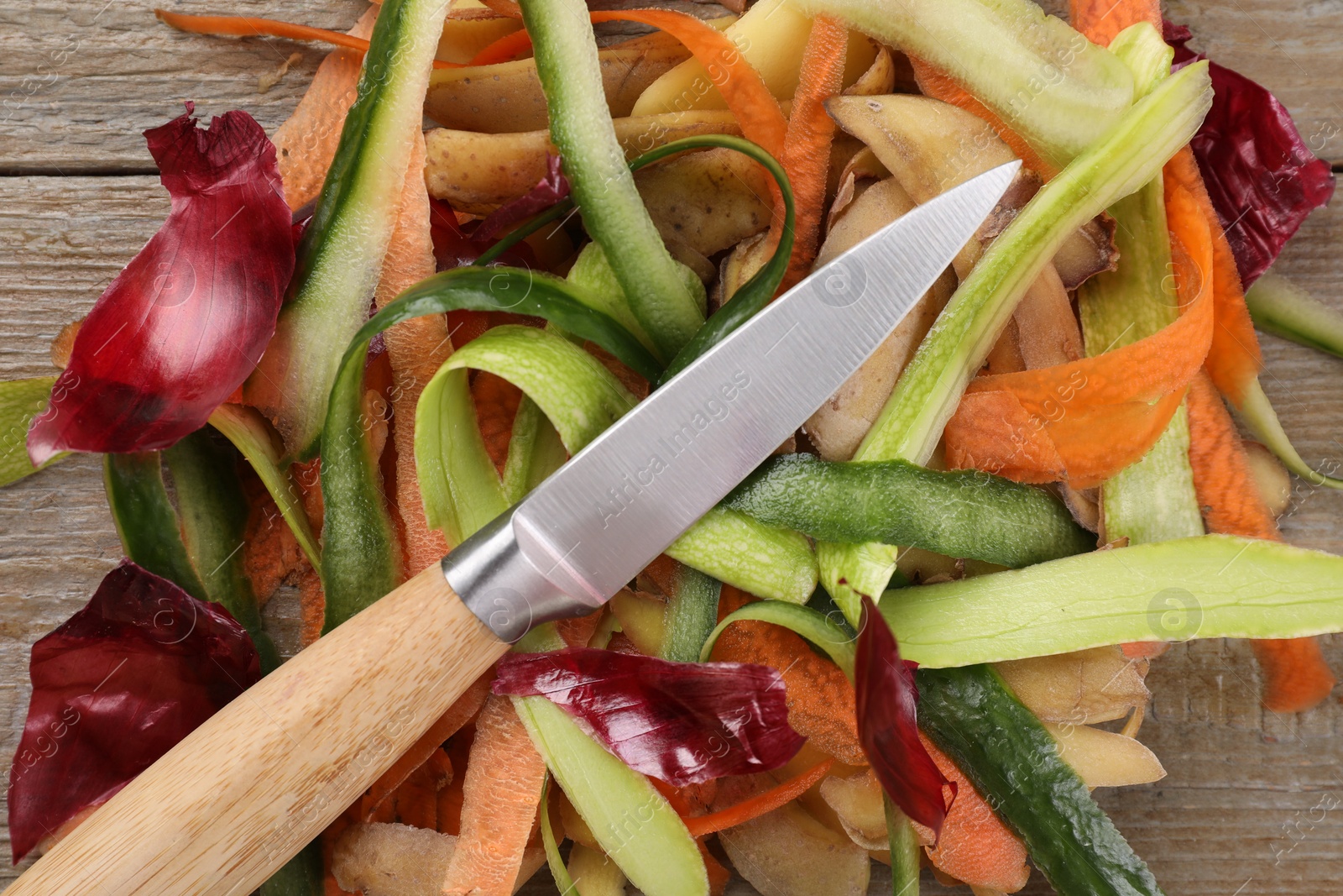 Photo of Peels of fresh vegetables and knife on wooden table, top view