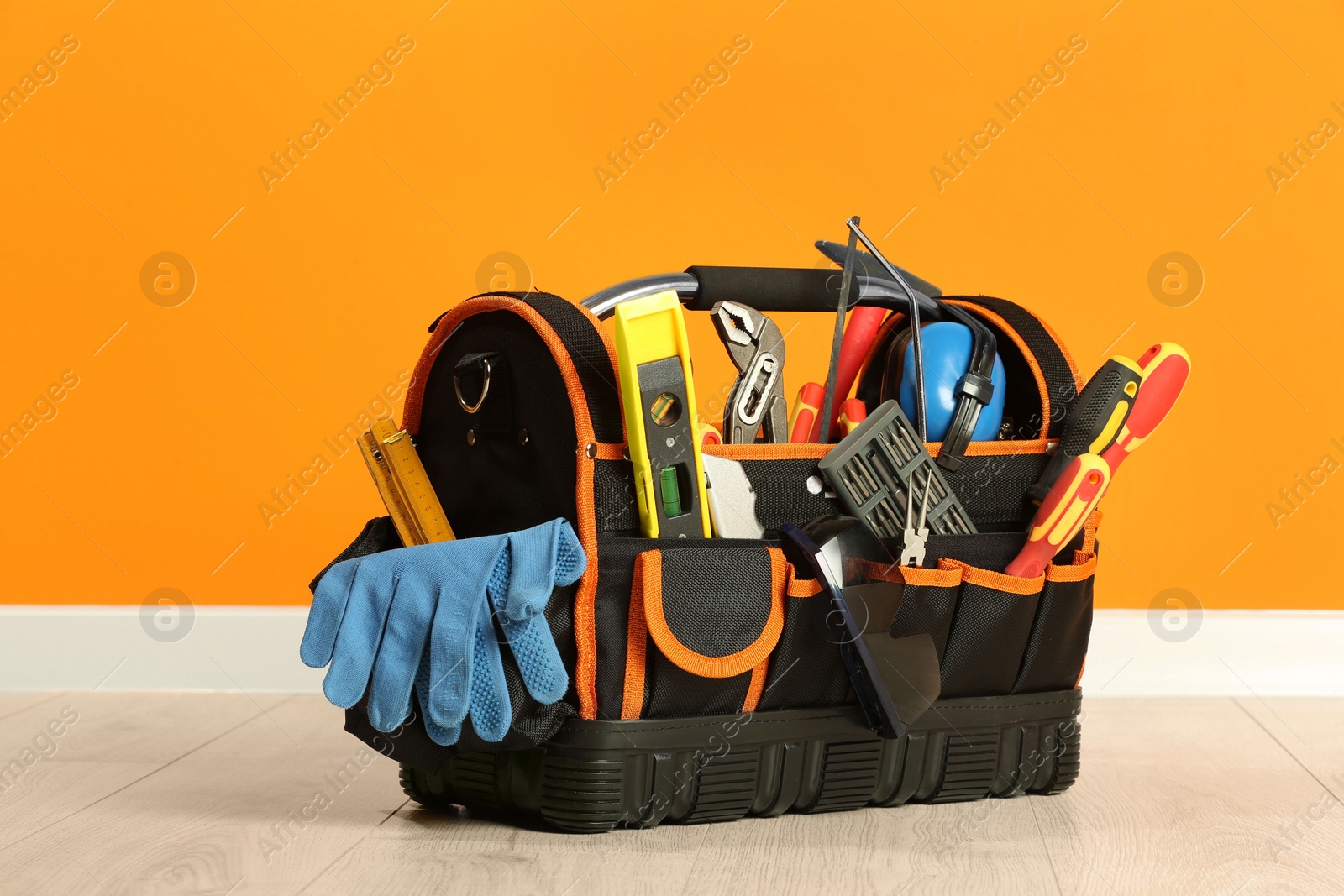 Photo of Bag with different tools for repair on floor near orange wall