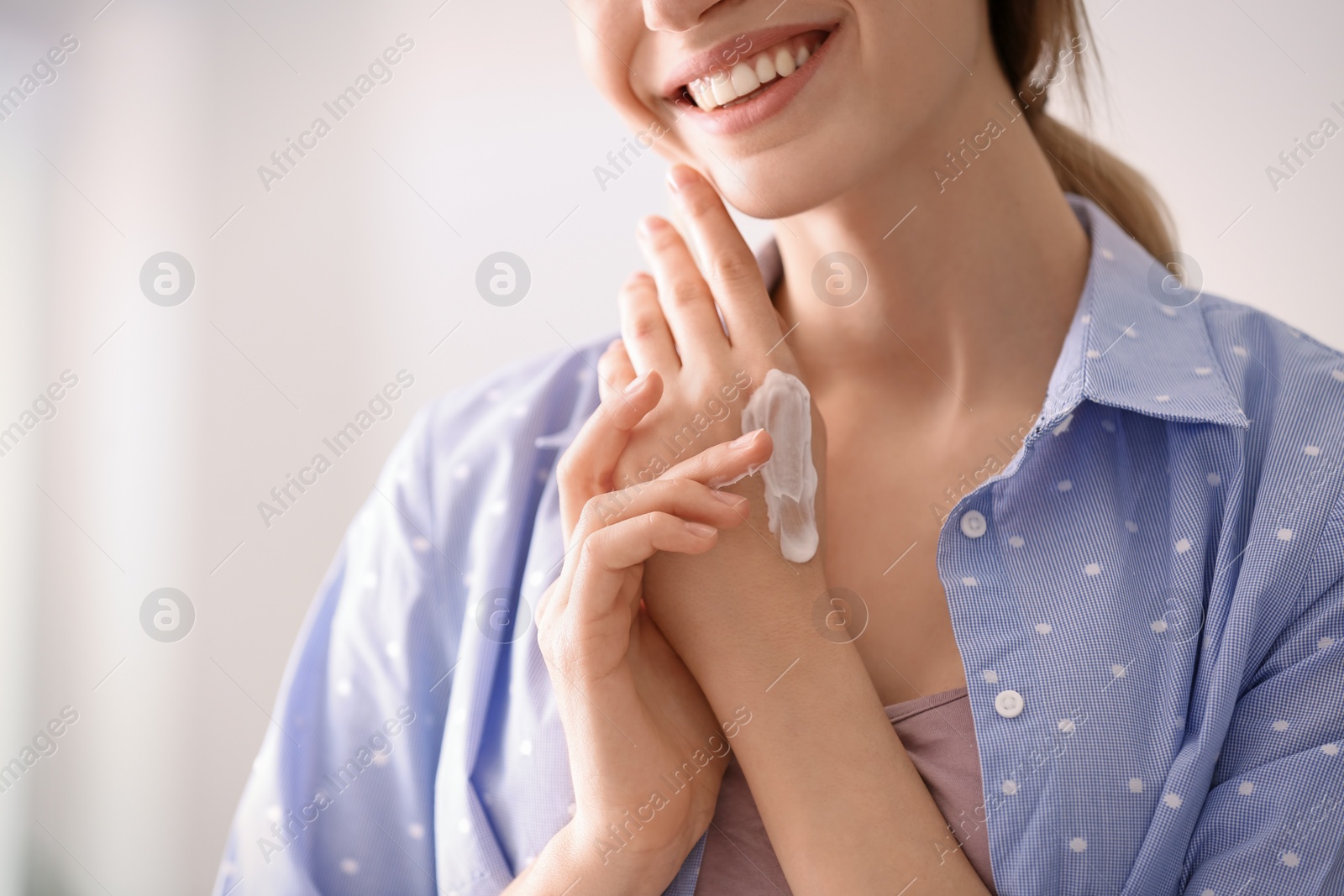 Photo of Young woman applying hand cream at home, closeup